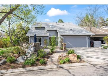 Inviting gray home featuring a stone waterfall feature, lush landscaping, and an attached two-car garage at 7126 Cedarwood Cir, Boulder, CO 80301