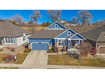 Charming blue home featuring a two-car garage, stone accents, and a cozy front porch with rocking chairs at 12957 W 78Th Cir, Arvada, CO 80005