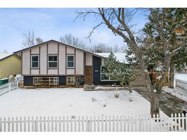 Ranch style home with a fenced yard, snow covered lawn, and mature trees at 15895 E 17Th Pl, Aurora, CO 80011