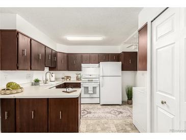 Well-lit kitchen with dark wood cabinets, white appliances, and a patterned rug at 3450 S Poplar St # 109, Denver, CO 80224