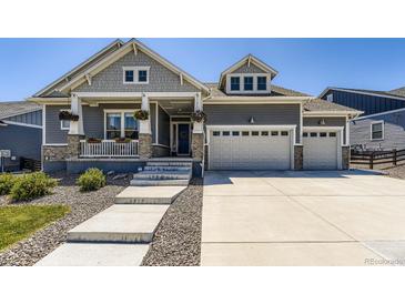 Charming two-story home featuring a welcoming front porch, gray siding, stone accents and a three car garage at 3344 Carabiner St, Castle Rock, CO 80108