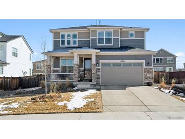 Two-story home with stone accents, gray siding, covered porch, and attached two-car garage at 12264 Olive Way, Thornton, CO 80602