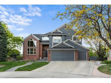 Two-story home features brick and gray siding with a three car garage and manicured lawn at 7411 S Crescent Ct, Littleton, CO 80120