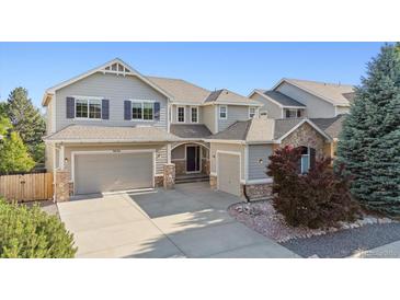Charming two-story home featuring gray siding, stone accents, a well-manicured lawn, and attached three-car garage at 9636 W 71St Pl, Arvada, CO 80004