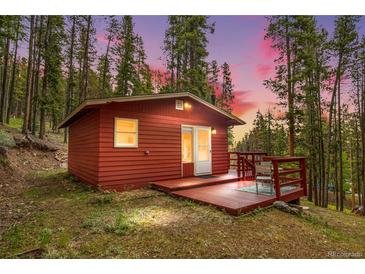 Charming red cabin nestled in a forest setting with a cozy deck, perfect for enjoying nature at 154 Apache Rd, Evergreen, CO 80439