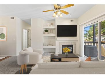 Bright living room with a fireplace, built-in shelves, ceiling fan, and sliding glass doors to a balcony at 10784 W 63Rd Pl # 205, Arvada, CO 80004