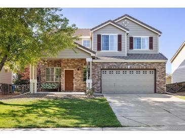 Charming two-story home with a brick facade, inviting porch swing, well-kept lawn, and a two-car garage at 14828 E 118Th Pl, Commerce City, CO 80603