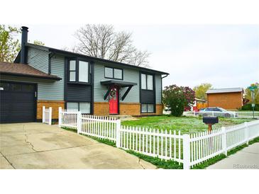 Charming two-story home with gray siding, red door, brick accents and a white picket fence creating a welcoming curb appeal at 1528 Coronado Pkwy, Denver, CO 80229