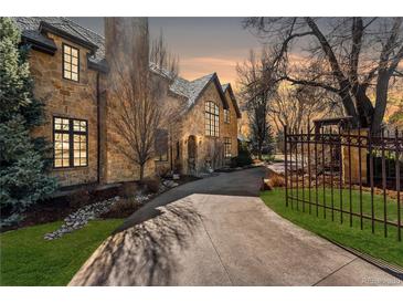 Stone home featuring a long driveway, manicured lawn, and mature trees under a colorful sunset at 4160 S Humboldt St, Cherry Hills Village, CO 80113
