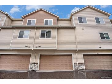 Exterior view of tan townhomes with attached garages featuring stone accents and neutral trim at 11250 Florence St # 29D, Commerce City, CO 80640