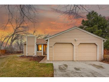 Tan home featuring an attached two-car garage, front lawn, and mature trees under a colorful dusk sky at 11623 W Hornsilver Mtn, Littleton, CO 80127