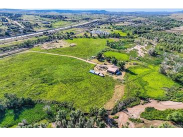 Expansive aerial view of a farm with large grassy fields, outbuildings, and a stream winding through the landscape at 11475 Us Highway 85, Littleton, CO 80125