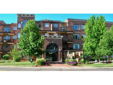 Brick apartment building with archway entrance, lush landscaping, balconies, and visible address at 2700 E Cherry Creek S Dr # 302, Denver, CO 80209