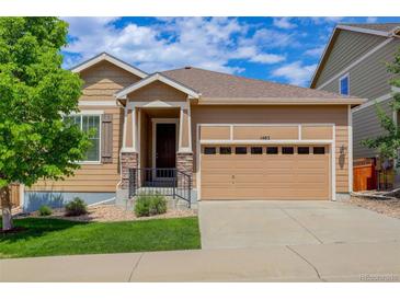 Charming tan-colored home with a two-car garage, a covered entry, and a well-manicured lawn at 1462 Raindrop Way, Castle Rock, CO 80109