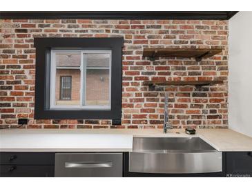 Modern kitchen features a stainless steel sink, exposed brick, and floating shelves at 3731 N Race St, Denver, CO 80205