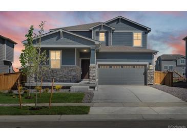 Charming two-story home with stone accents and a well-manicured lawn at dusk at 17487 E 89Th Way, Commerce City, CO 80022