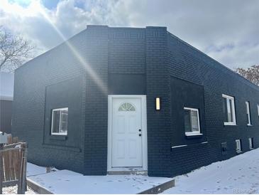 Charming house featuring a unique black brick exterior, complemented by a pristine white front door and snow-covered steps at 20 E 45Th Ave, Denver, CO 80216