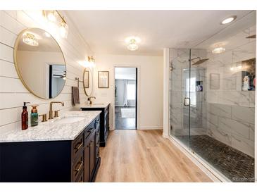 Bright bathroom with a dual sink vanity, marble countertops, modern fixtures, and a glass enclosed shower at 1786 Quartz St, Castle Rock, CO 80109