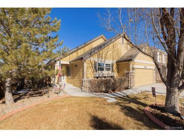 Charming yellow home featuring stone accents, an attached garage, a well-manicured lawn, and an American flag at 16102 Grebe Pl, Parker, CO 80134