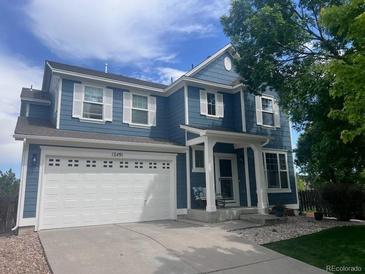 Charming blue two-story home featuring a pristine white garage door, shuttered windows, and a welcoming covered entryway at 12491 E 106Th Pl, Commerce City, CO 80022
