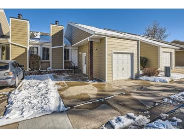 Tan siding townhouse with white door, attached garage, and snow-covered walkway at 11860 Harrison St, Thornton, CO 80233