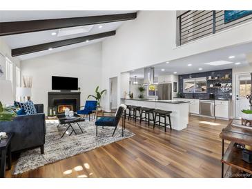 Open-concept living room with vaulted ceilings, dark beams, fireplace, and seamless transition to modern kitchen at 1835 S Poplar St, Denver, CO 80224