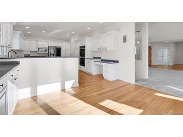 Bright kitchen features white cabinets, stainless appliances, hardwood floors, and modern design at 14032 E Chenango Dr, Aurora, CO 80015