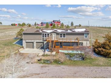 Split level home with two car garage, wooden deck and stairs with farm buildings in background at 40192 Margaret Dr, Elizabeth, CO 80107