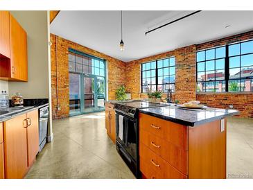 Bright, open kitchen features brick walls, stainless steel appliances, and a center island with a black countertop at 2500 Walnut St # 102, Denver, CO 80205