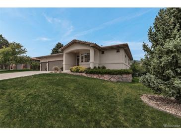 Beautiful stucco home featuring a well-maintained lawn, mature trees, and a stone garden bed at 6379 Spotted Fawn Run, Littleton, CO 80125