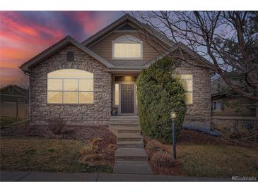 Charming stone-accented home with an arched window and professional landscaping under a colorful sky at dusk at 7033 S Versailles St, Aurora, CO 80016