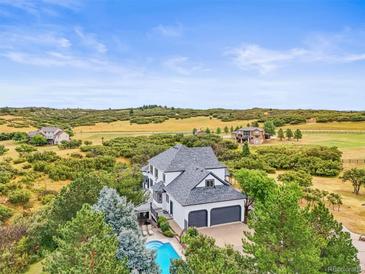 Stunning aerial view of a home with a pool and lush landscaping backing up to an open field at 1635 Sharps Ct, Castle Rock, CO 80109