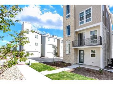 Modern three-story townhome with a stone accent tower, small balcony, and manicured lawn at 11205 W 53Rd Ln, Arvada, CO 80002