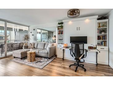Comfortable living area featuring a gray sectional sofa, hardwood floors, and a built-in Murphy bed with shelving and desk at 790 N Washington St # 1003, Denver, CO 80203