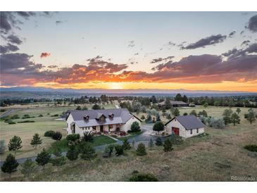 Stunning sunset view of stone home with large lot and separate garage, nestled in a picturesque landscape at 8456 N Sundown Trl, Parker, CO 80134