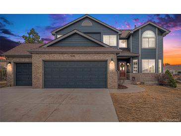 Charming two-story home with brick and blue siding, attached two-car garage and manicured front yard at sunset at 510 W Prestwick Way, Castle Rock, CO 80104