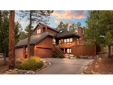 Stunning wood home with a deck, mature trees, stone accents, and a long driveway at 29857 Park Village Dr, Evergreen, CO 80439