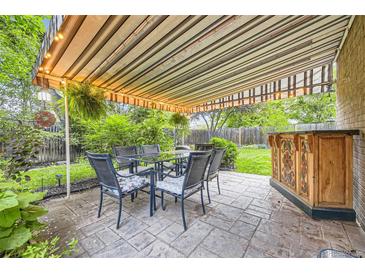 Outdoor patio area featuring a bar, stone tile floor, and seating under a retractable awning, surrounded by lush greenery at 1640 Pontiac St, Denver, CO 80220