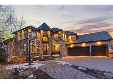 Stunning stone house with three-car garage, basketball hoop, and manicured front yard, illuminated by twilight at 5810 Amber Ridge Dr, Castle Pines, CO 80108