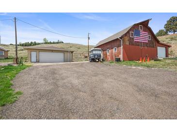 Spacious red barn with an American flag and a detached garage on a large lot with a gravel driveway at 12101 Riverdale Rd, Brighton, CO 80602