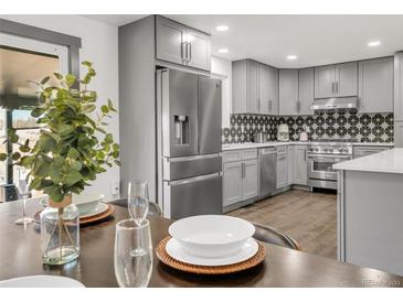 Modern kitchen with gray cabinets, stainless steel appliances, patterned backsplash, and hardwood floors at 8331 Oakwood St, Westminster, CO 80031