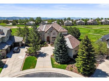 An aerial view of a landscaped two-story home, with a circular driveway, on a golf course near the mountains at 1287 Buffalo Ridge Rd, Castle Pines, CO 80108