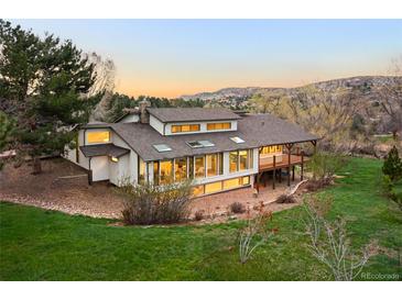 Expansive home featuring walls of windows, a deck, mature trees and a well-maintained lawn at 6491 Crestbrook Dr, Morrison, CO 80465