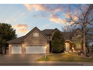 Beautiful stone home featuring a three-car garage and meticulously maintained landscaping under a dynamic, colorful sky at 21231 E Saddle Rock Ln, Aurora, CO 80016
