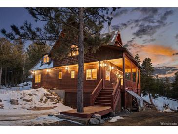 Charming wood home with a covered porch, lush evergreens, and snow-covered yard at dusk at 439 Ronnie Rd, Golden, CO 80403