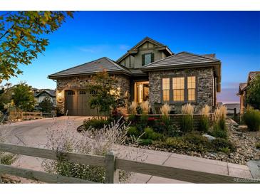 Charming stone home with a well-manicured front yard and a curved driveway at dusk at 10731 Featherwalk Ln, Highlands Ranch, CO 80126