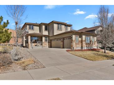 A tan two-story home with a three-car garage, brick accents, and a concrete driveway under a blue sky at 24269 E Arapahoe Pl, Aurora, CO 80016