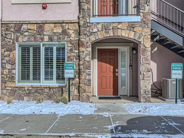 Stone accented condo with red door, reserved parking, and snow on the ground at 15195 E 16 Th Pl # 104, Aurora, CO 80011