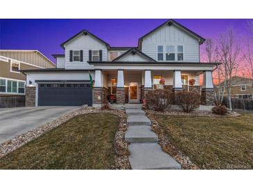 Charming two-story home featuring a covered porch, gray siding, stone accents, and an attached two-car garage at 2342 Hickory Pl, Erie, CO 80516