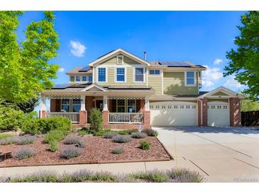 Inviting two-story home featuring a charming front porch, lush landscaping, and solar panels on the roof at 21395 E Greenwood Pl, Aurora, CO 80013